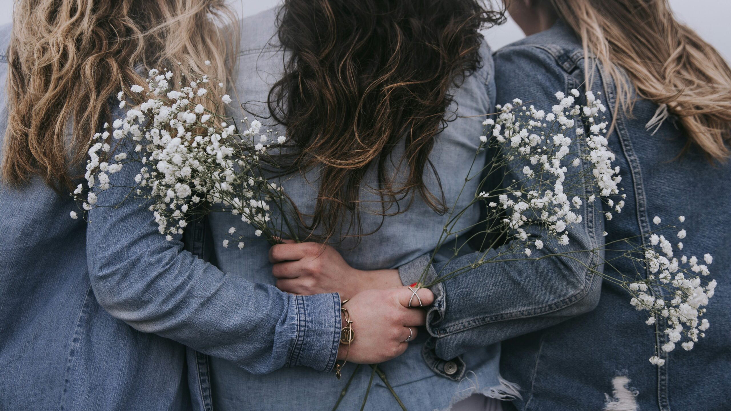 group of women with their backs toward us, holding flowers and with arms around each other 